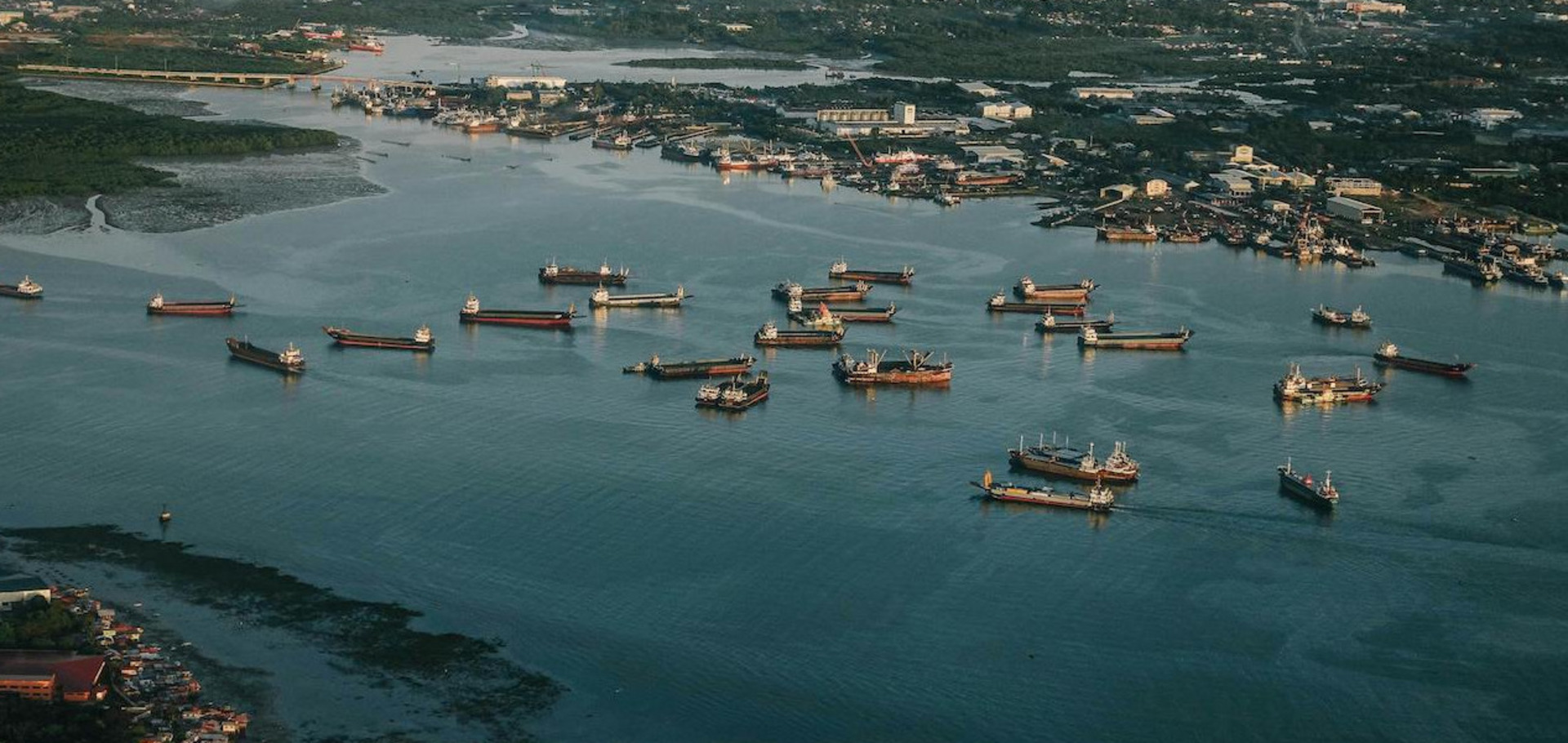 Eine Luftaufnahme von mehreren Containerschiffen, die auf ruhigen Gewässern in einem Hafen nebeneinander liegen.