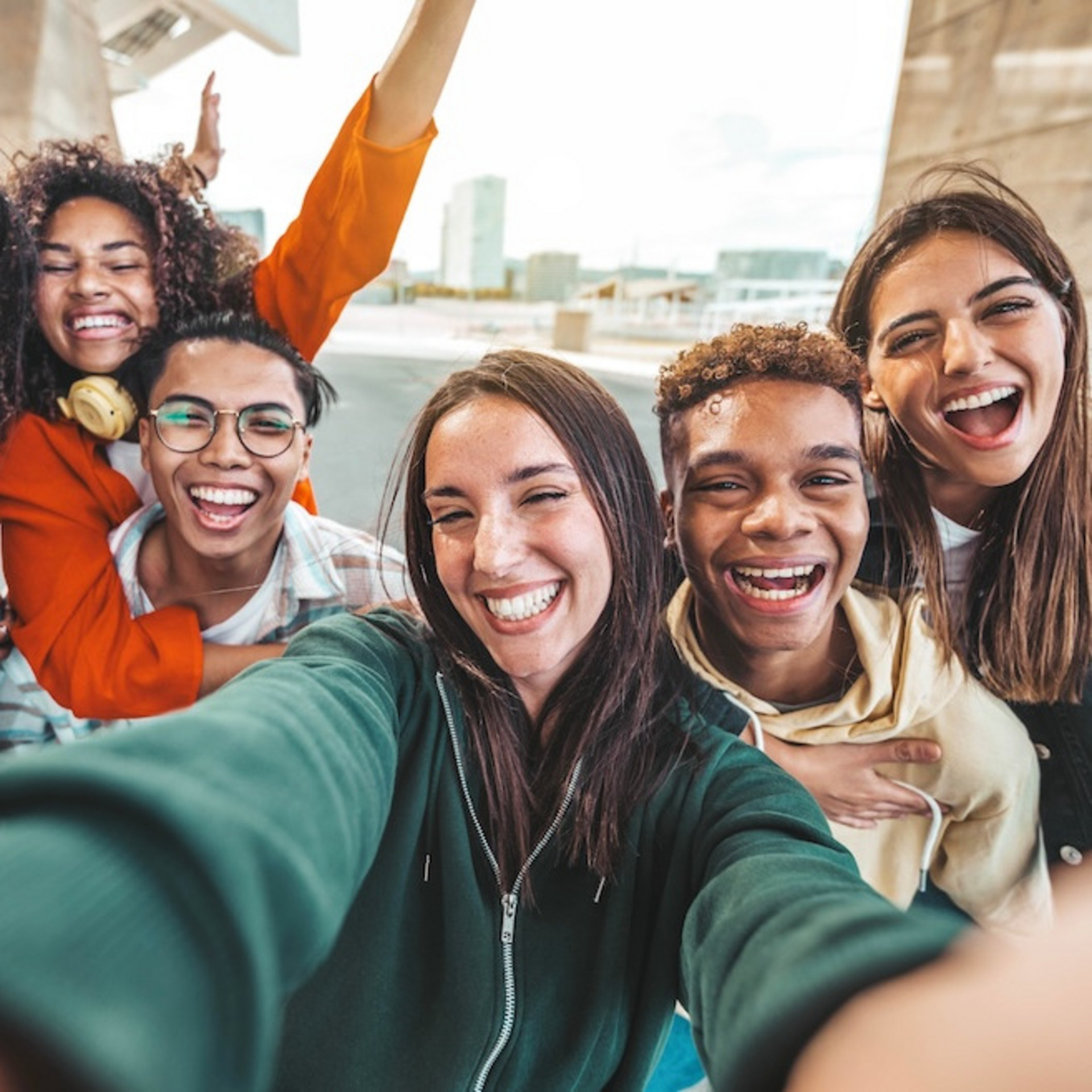 Eine Gruppe von sieben fröhlichen jungen Menschen macht ein Selfie, im Hintergrund ist die Kulisse einer Stadt zu sehen