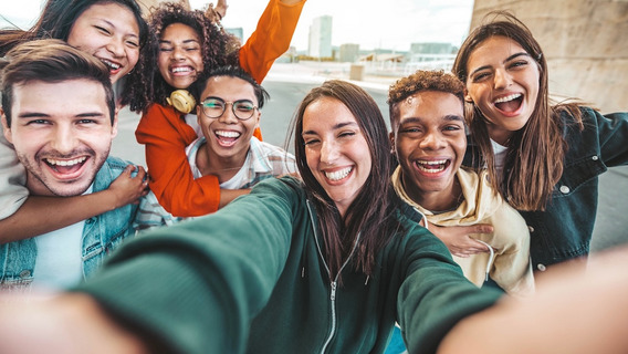 Eine Gruppe von sieben fröhlichen jungen Menschen macht ein Selfie, im Hintergrund ist die Kulisse einer Stadt zu sehen