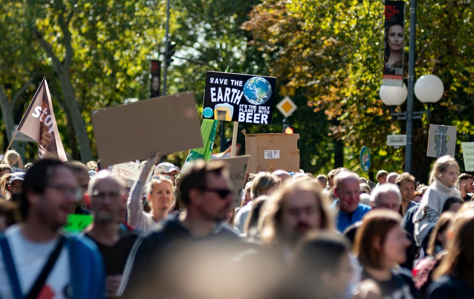 Eine große Menschenmenge protestiert auf der Straße. Viele von ihnen halten Schilder hoch, darunter ein Schild mit der Aufschrift "Save the Earth. It's the only planet with beer".