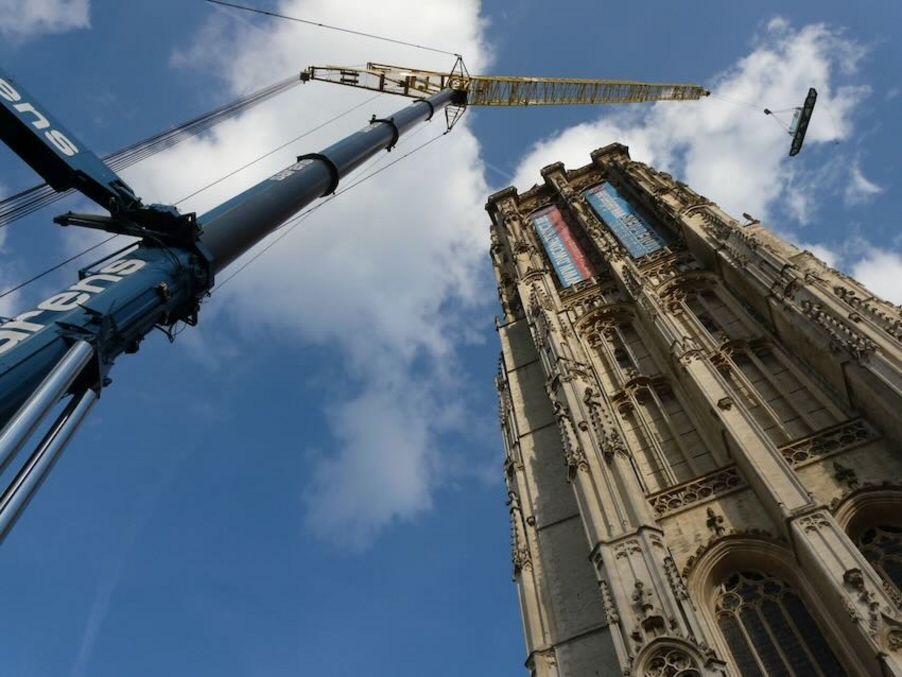 Eine hohe gotische Kathedrale – die berühmte St.-Rombouts-Kathedrale in Mechelen – mit einem Kran im Vordergrund. Der Blickwinkel von unten nach oben lässt die Architektur des Gebäudes besonders beeindruckend wirken.