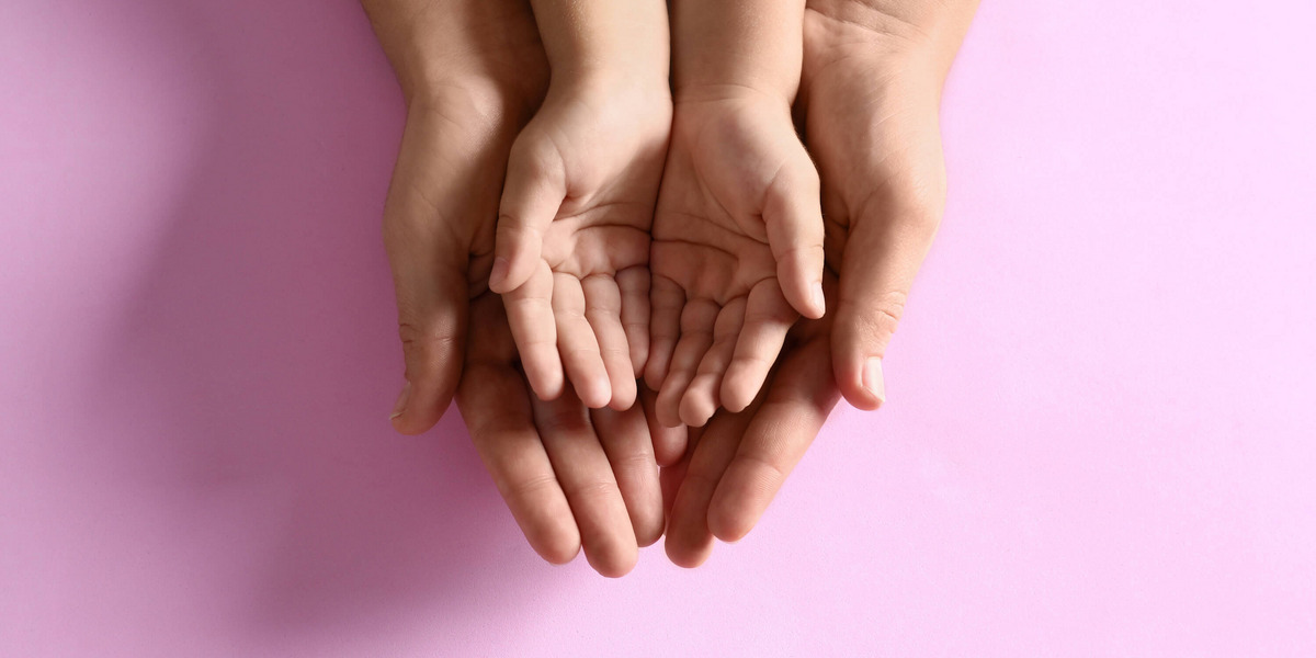 Kinderhände liegen in größeren Händen auf rosa Hintergrund