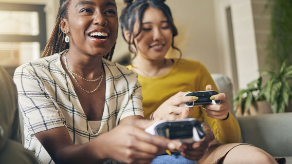 Zwei junge Frauen sitzen mit Spielekonsole auf dem Sofa