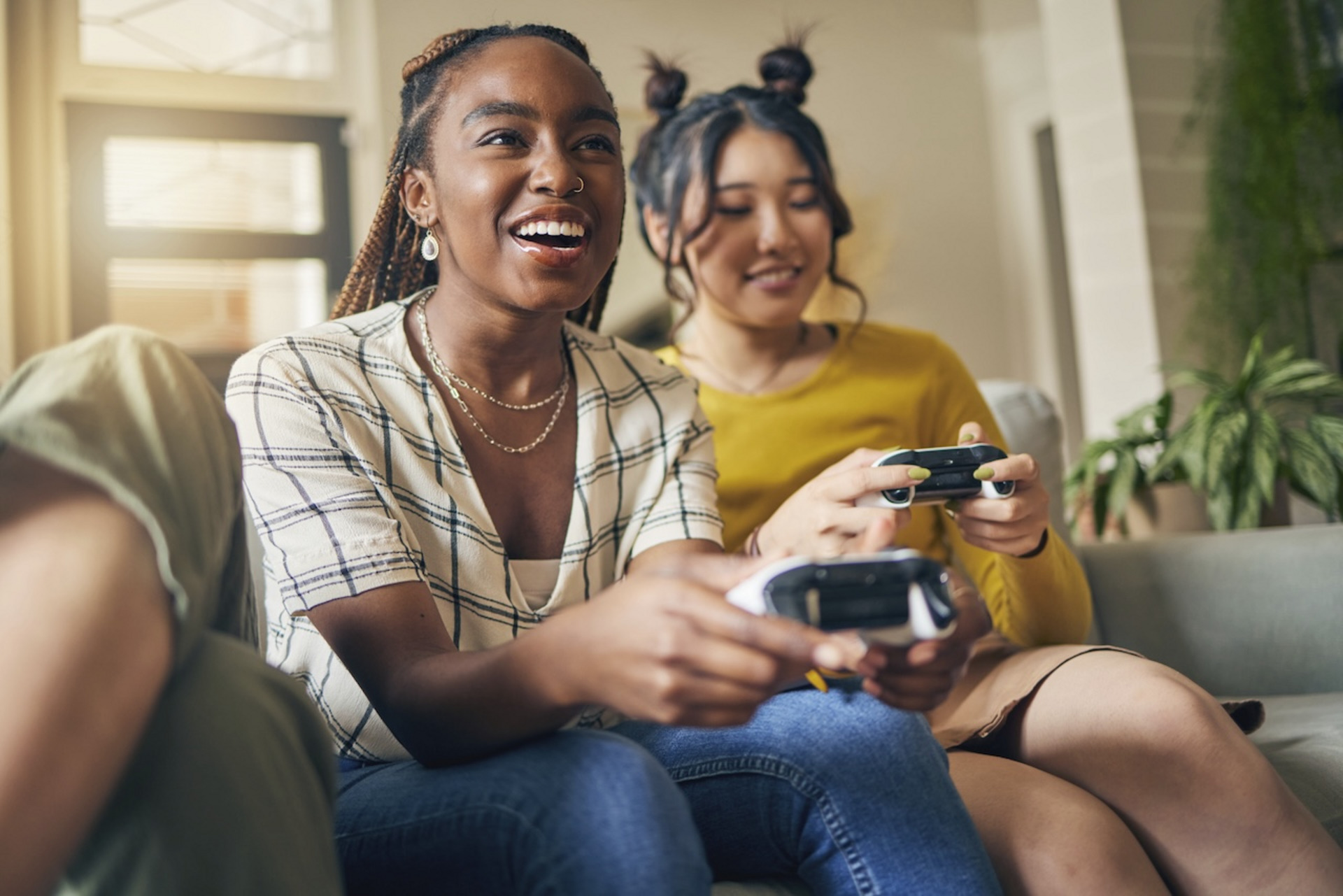 Zwei junge Frauen sitzen mit Spielekonsole auf dem Sofa