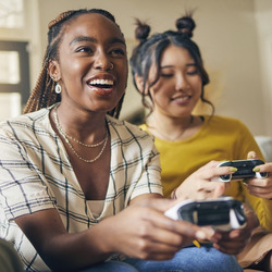 Zwei junge Frauen sitzen mit Spielekonsole auf dem Sofa