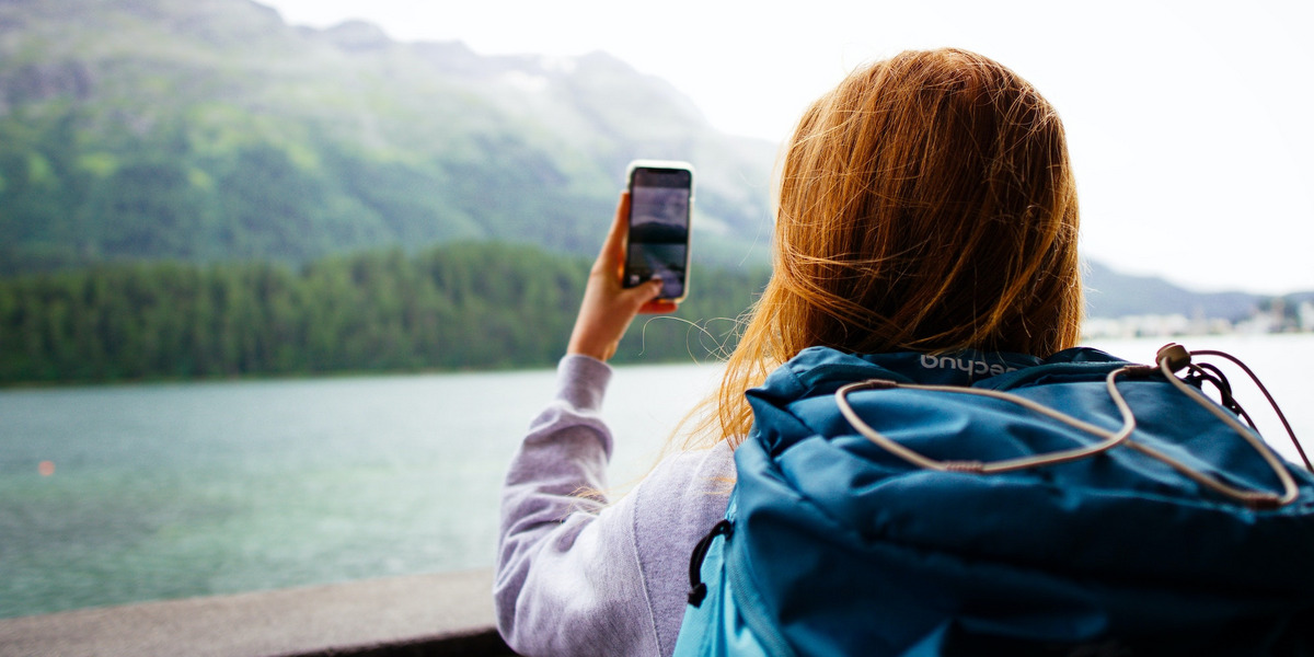 Eine junge Frau steht vor einer Bergkulisse und macht ein Foto