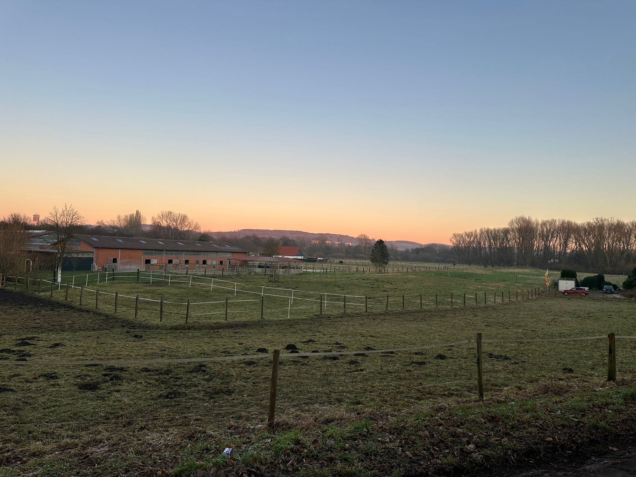 Zu sehen sind winterliche Wiesen, ein Reiterhof und Wälder im Hintergrund